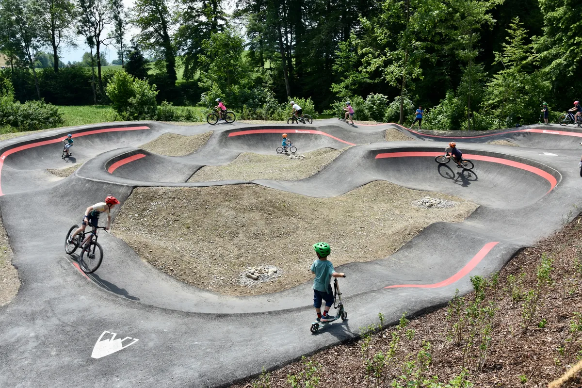 Über einen solchen Pumptrack wie bei der Sportanlage Hüssenbüel in Hinwil wird auch die Gemeinde Wald bald verfügen. Kinder fahren mit Fahrrädern und Scootern über eine betonierte Piste.